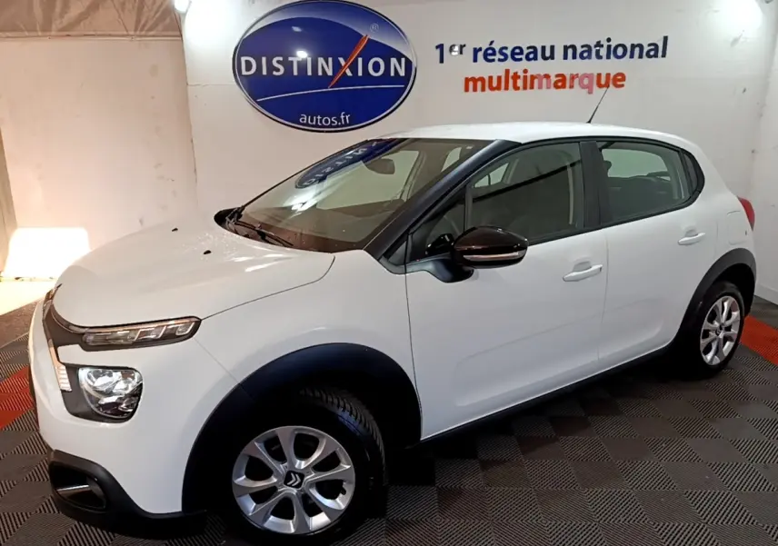 Vue 3/4 avant droit d'une Citroën C3 blanche avec protections noires et jantes alliage en showroom.