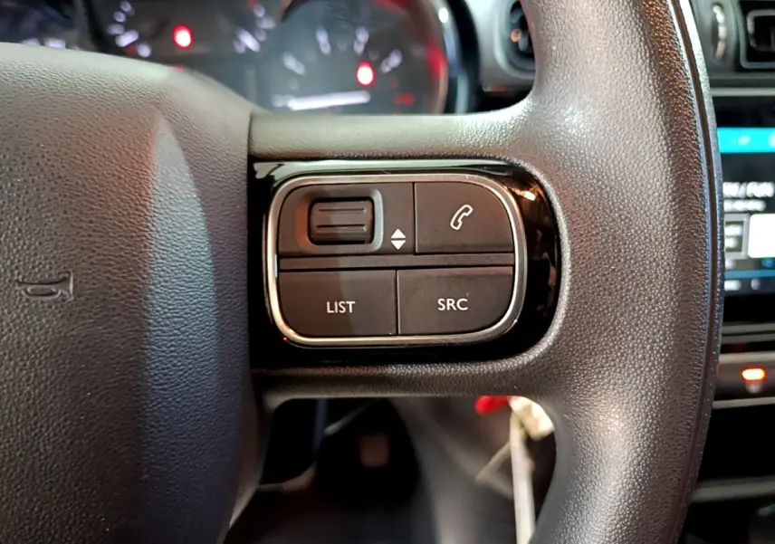 Gros plan sur les commandes du volant à droite d’une Citroën C3 blanche, avec boutons de téléphone et liste.