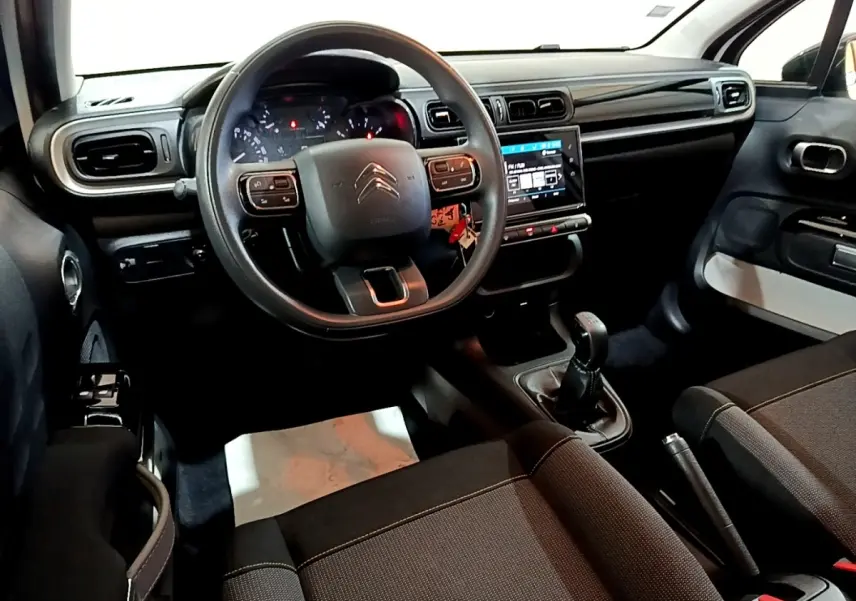 Vue intérieure de face du poste de conduite de la Citroën C3 blanche, avec volant multifonctions et écran tactile central.