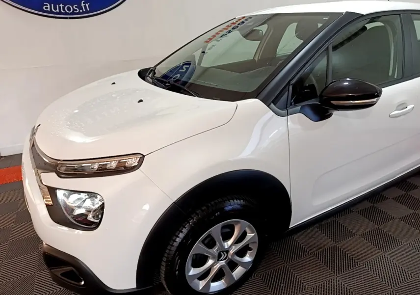 Vue 3/4 avant droit d'une Citroën C3 blanche avec rétroviseurs noirs et jantes alliage argentées.