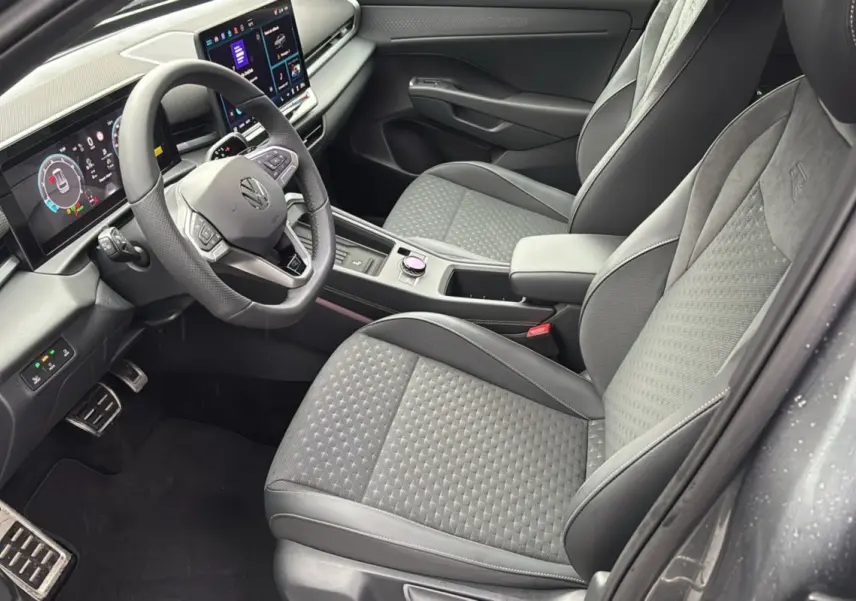 Vue intérieure côté conducteur du Volkswagen T-Roc 2026, sièges tissu gris avec volant cuir multifonctions et tableau de bord digital.