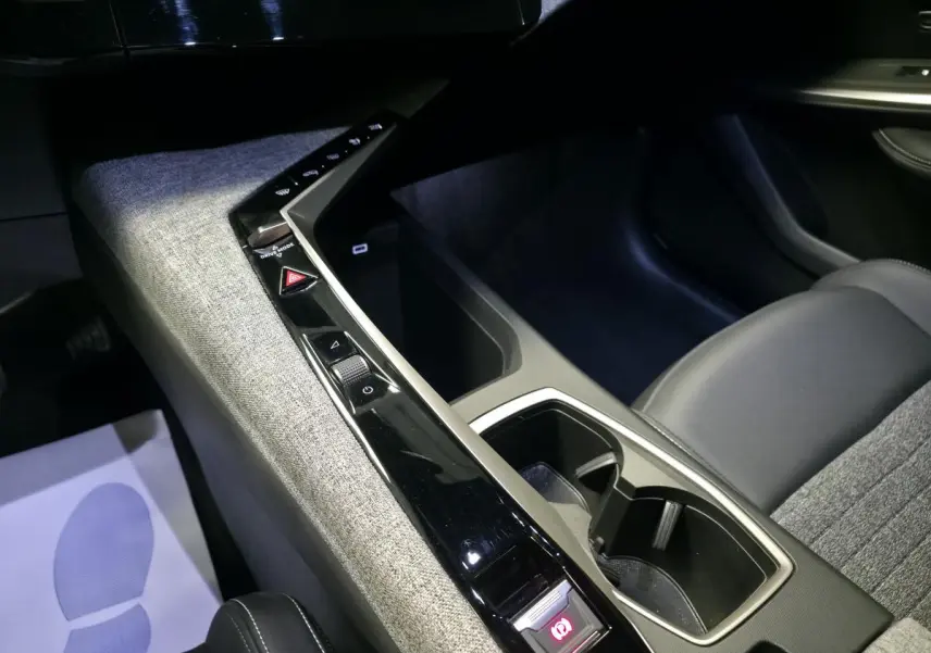Vue intérieure rapprochée de la console centrale tissu gris et noir laqué du Peugeot 3008 Hybrid 2025.