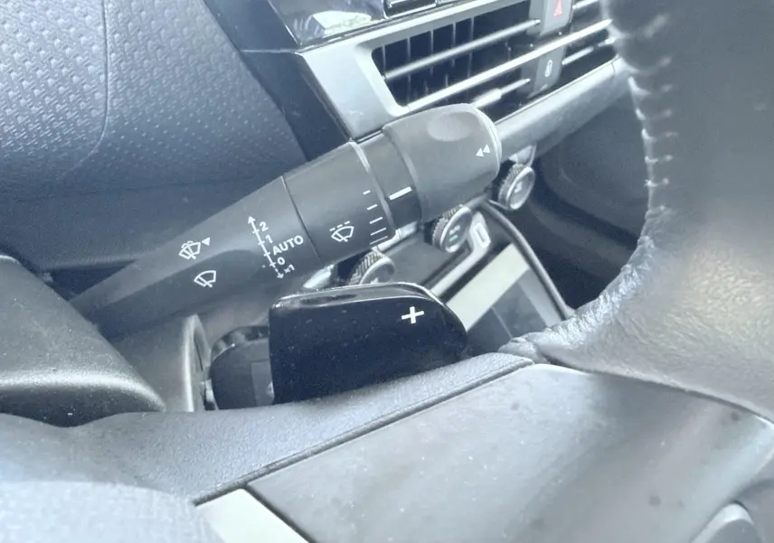 Gros plan sur la commande de régulateur de vitesse et levier d'essuie-glace dans l'habitacle gris-noir d'une Citroën C4 blanche.