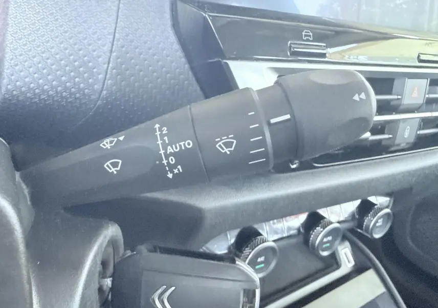 Gros plan sur la commande d’essuie-glace à gauche du volant dans l’habitacle gris noir d’une Citroën C4 blanche.