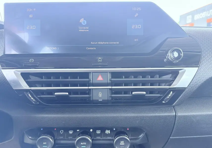Vue frontale du tableau de bord de la Citroën C4 blanche 2023, avec écran tactile et commandes de climatisation visibles.