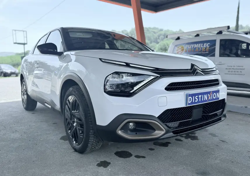 Vue 3/4 avant gauche d'une Citroën C4 blanche avec calandre distinctive et jantes noires sous abri.