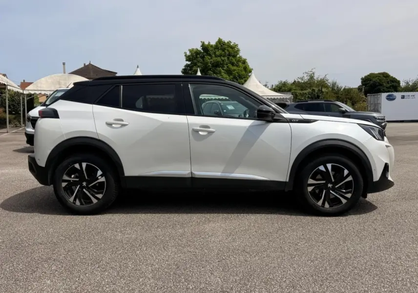 Profil droit d’un Peugeot 2008 blanc 2021 avec toit noir et jantes alliage noires, stationné en extérieur.