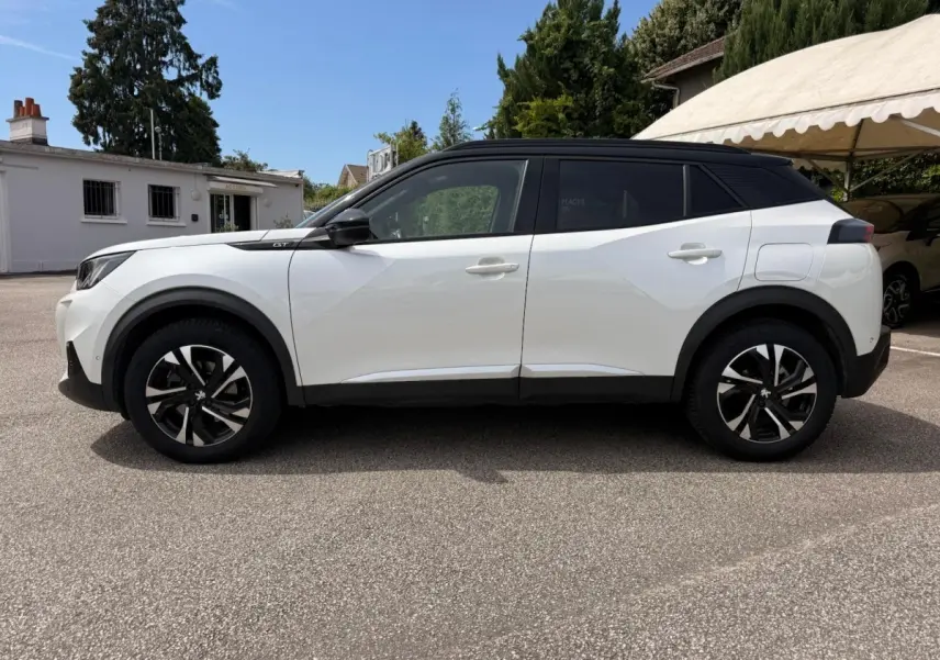 Vue de profil côté gauche d’un Peugeot 2008 blanc avec toit noir et jantes alliage noires, stationné en extérieur.