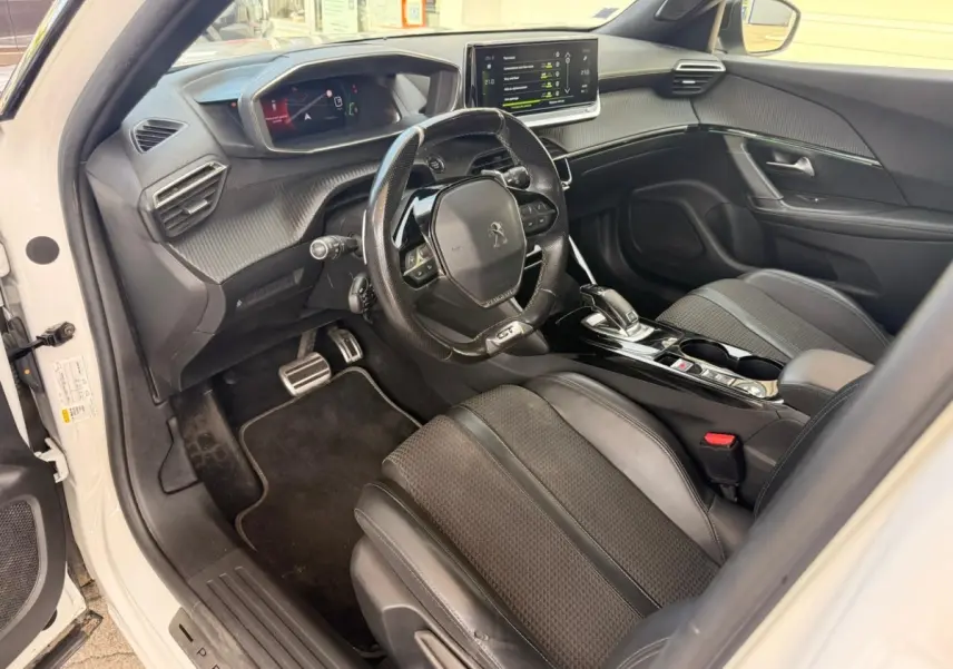 Vue intérieure côté conducteur du Peugeot 2008 blanc, mettant en valeur le volant GT, la sellerie tri-matière et l'écran tactile central.