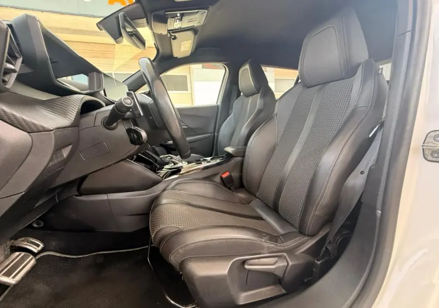 Vue intérieure côté conducteur du Peugeot 2008 blanc 2021, mettant en valeur les sièges sport en tissu et cuir noir.