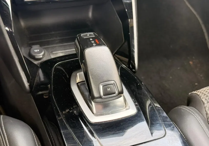 Gros plan sur la commande de boîte automatique noire au centre de la console d’une Peugeot 2008 blanche, intérieur sombre.