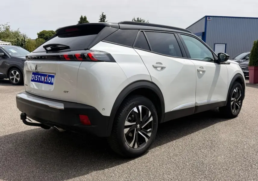 Vue 3/4 arrière droite d’un Peugeot 2008 blanc avec toit noir et jantes alliage distinctives, stationné en extérieur.