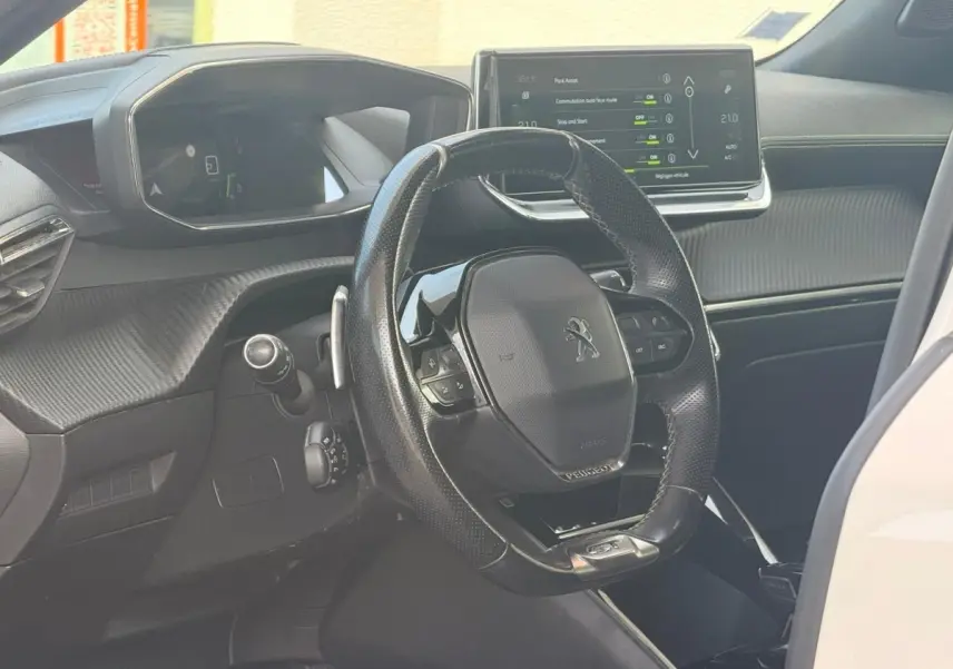 Vue intérieure du poste de conduite du Peugeot 2008 blanc, avec volant compact et écran tactile central visible.