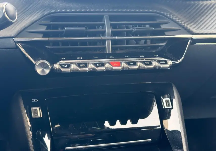 Gros plan sur la console centrale noire brillante du Peugeot 2008 1.5 BlueHDi 130ch, avec commandes et prises USB visibles.