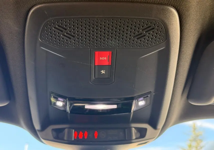 Vue en contre-plongée du plafonnier intérieur noir du Peugeot 2008 blanc, avec bouton SOS rouge et éclairage LED allumé.