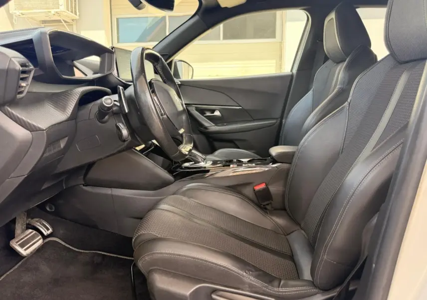 Vue intérieure côté conducteur du Peugeot 2008 blanc, mettant en valeur les sièges noirs en tri-matière avec surpiqûres et le volant cuir.