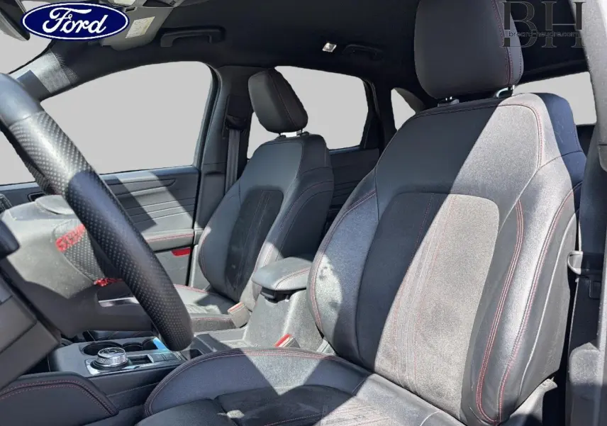 Vue intérieure côté conducteur du Ford Kuga 2024, sièges sport en suédine grise avec surpiqûres rouges visibles.