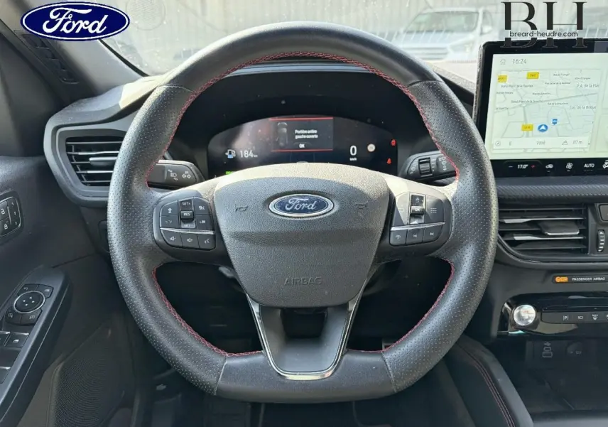 Vue intérieure centrée sur le volant sport noir à surpiqûres rouges du Ford Kuga 2024 avec tableau de bord numérique et écran tactile GPS.