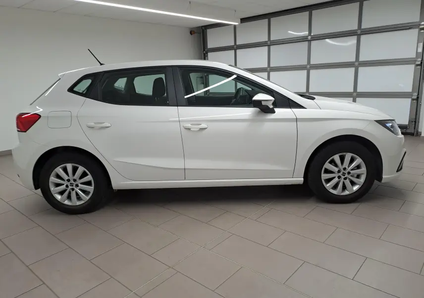 Vue de profil côté gauche d'une SEAT Ibiza blanche Candy 2023, finition Style Business, en intérieur sur sol carrelé.