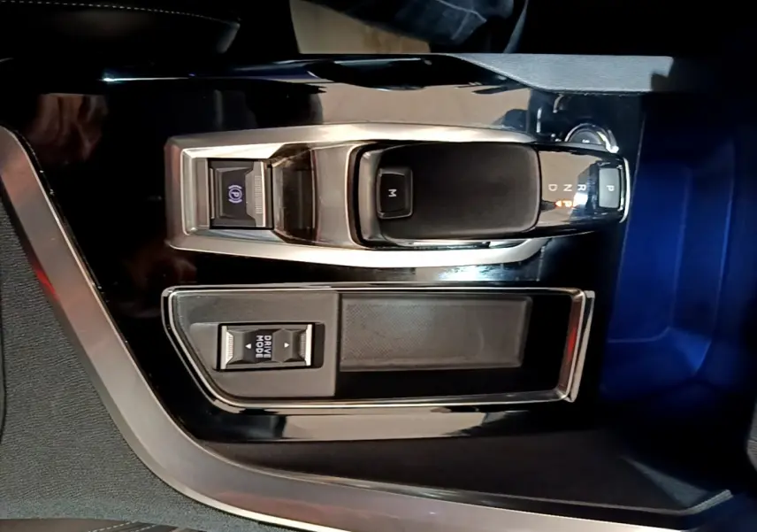 Vue rapprochée de la console centrale noire brillante avec levier de vitesse automatique et bouton mode conduite du Peugeot 3008 gris foncé.