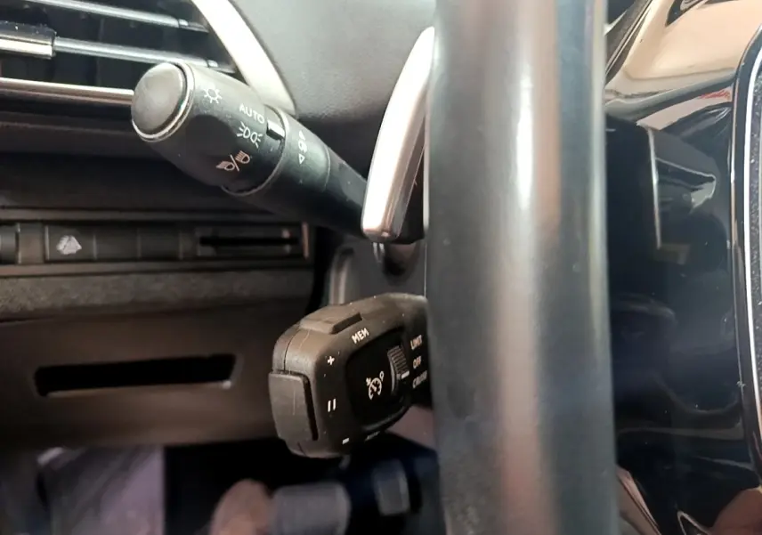 Gros plan sur la commande de régulateur de vitesse et levier d'éclairage côté gauche du volant cuir noir du Peugeot 3008 gris foncé.