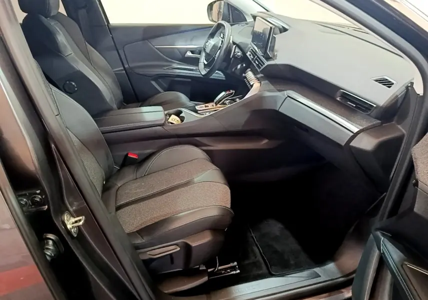 Intérieur avant droit du Peugeot 3008 2022 gris foncé, sièges tissu et cuir, tableau de bord avec écran tactile central.