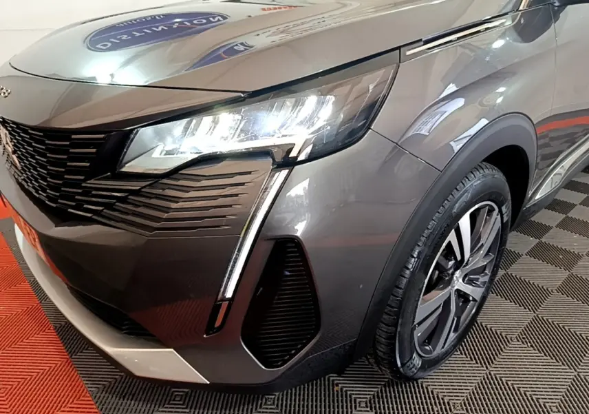 Gros plan sur l'avant droit du Peugeot 3008 gris foncé 2022, mettant en valeur ses phares LED et la calandre distinctive.