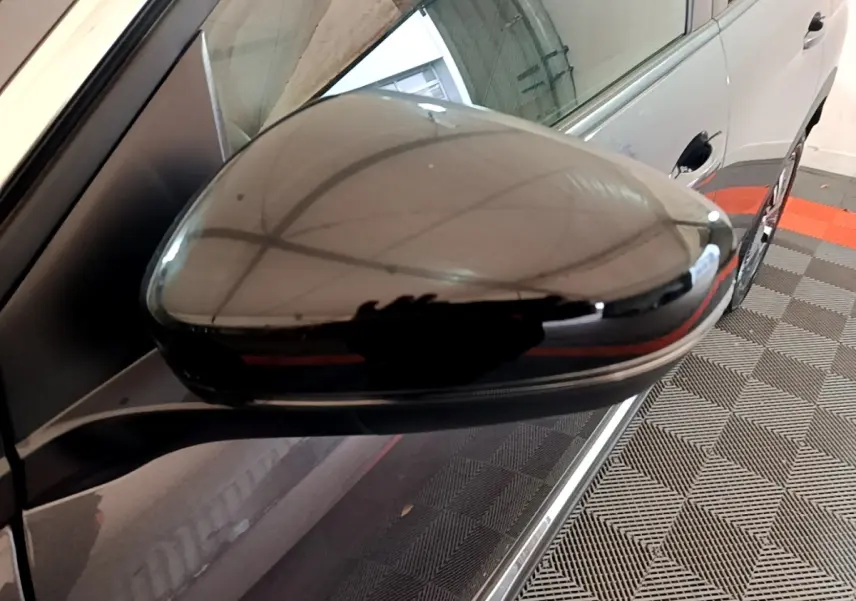 Rétroviseur droit noir brillant du Peugeot 3008 gris foncé, vue rapprochée avec reflet du plafond du garage.