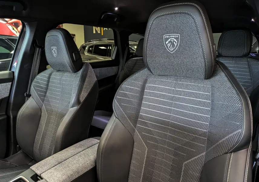 Gros plan sur les sièges avant en tissu gris et cuir noir du Peugeot 5008 Hybrid 145 GT avec logo Peugeot brodé sur les appuie-têtes.