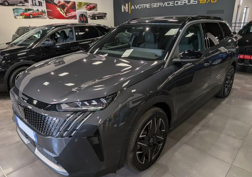 Peugeot 5008 Hybrid 145 GT gris titane avec toit noir, vue 3/4 avant droit en intérieur showroom.