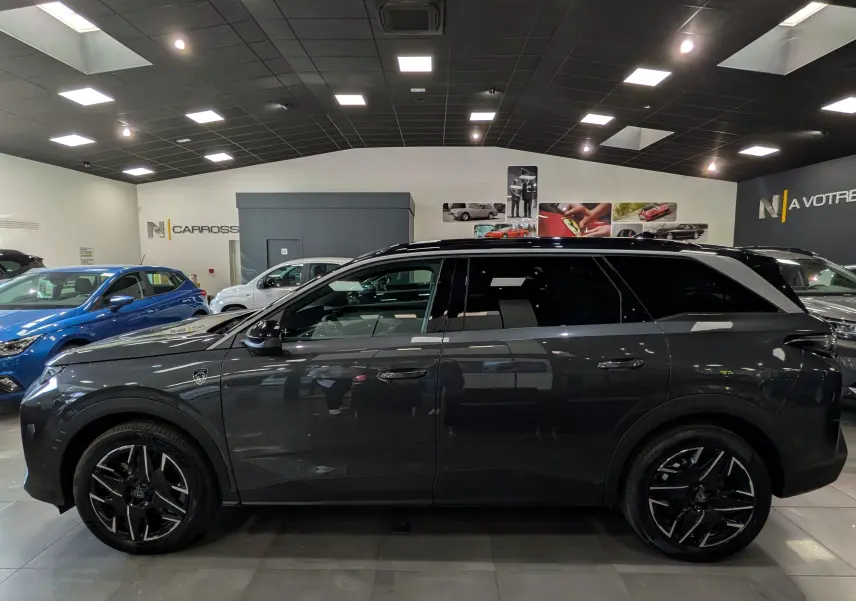 Vue de profil côté gauche d’un Peugeot 5008 Hybrid gris titane avec toit noir et jantes noires en concession.