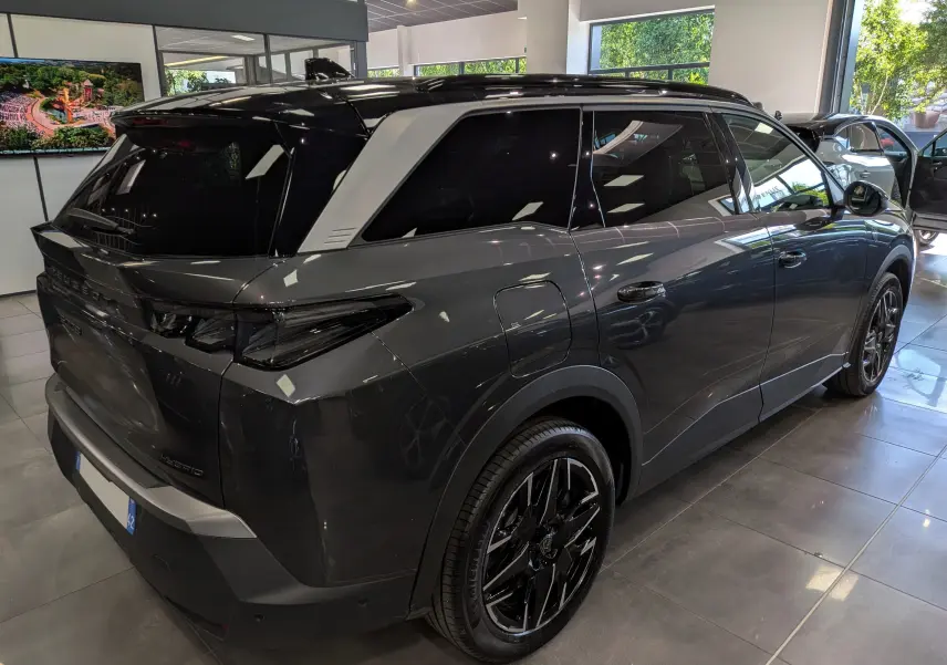 Vue 3/4 arrière droite du Peugeot 5008 Hybrid gris titane avec toit noir et jantes noires en showroom.