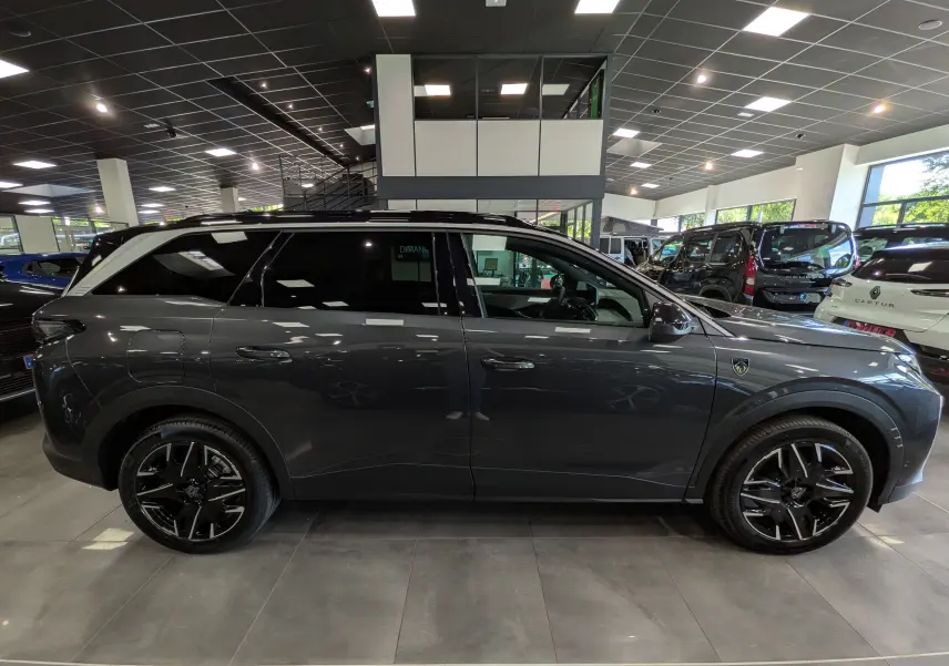 Vue de profil côté droit du Peugeot 5008 Hybrid gris titane avec toit noir et jantes noires en concession.