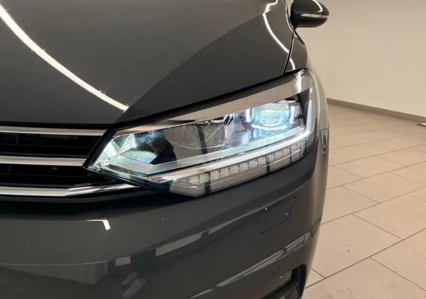 Gros plan sur le phare avant droit du Volkswagen Touran 2025 gris dauphin avec peinture métallisée brillante.