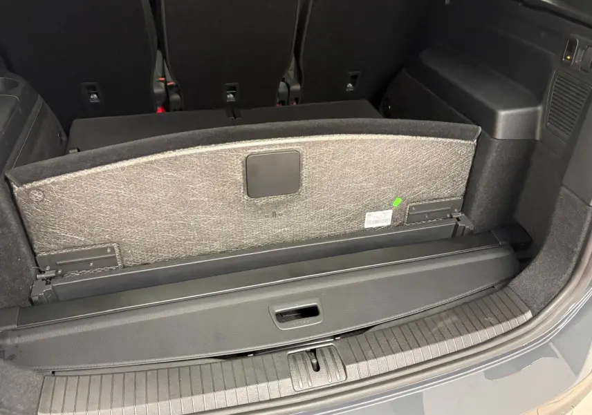 Coffre ouvert du Volkswagen Touran gris dauphin, montrant la banquette arrière et le cache-bagages rétractable.