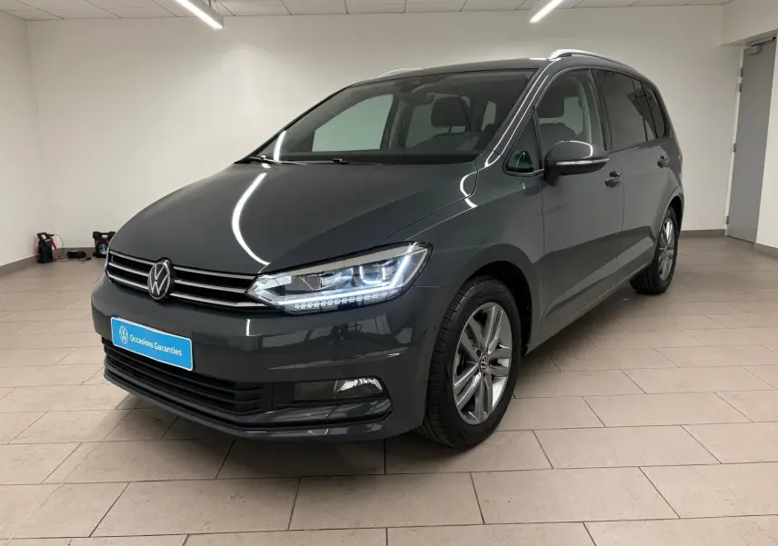 Vue 3/4 avant droit d’un Volkswagen Touran gris dauphin métallisé, avec feux LED allumés en intérieur neutre.