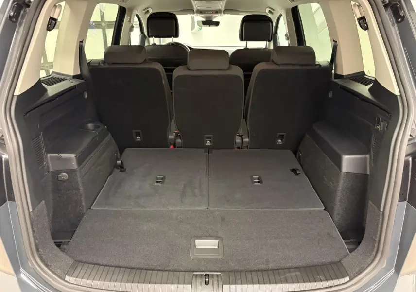 Vue arrière du coffre ouvert du Volkswagen Touran gris dauphin, sièges arrière partiellement rabattus et espace de chargement spacieux.