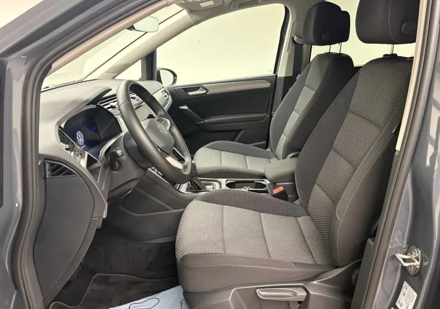 Vue intérieure côté conducteur du Volkswagen Touran gris dauphin, montrant les sièges avant et le tableau de bord moderne.