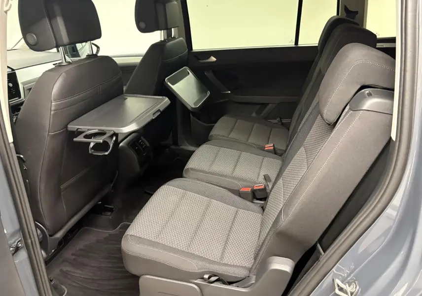 Vue latérale droite de l'intérieur arrière du Volkswagen Touran gris Dauphin avec tablette rabattable et sièges tissu gris.