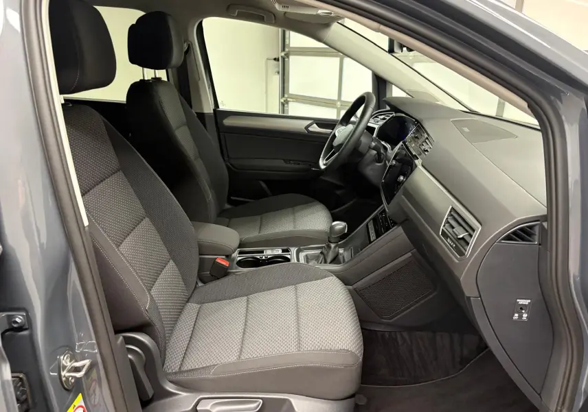Vue intérieure côté conducteur du Volkswagen Touran gris dauphin, montrant les sièges et le tableau de bord moderne.
