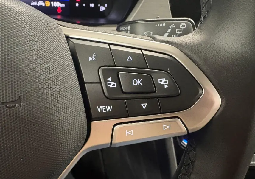 Gros plan sur les commandes multifonctions au volant du Volkswagen Touran 2025, finition VW Edition, avec boutons noirs et contour argenté.