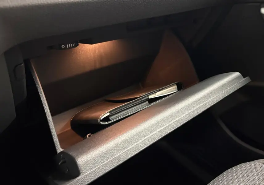 Gant de boîte à gants ouvert avec éclairage intérieur, montrant un carnet noir dans un Volkswagen Touran gris Dauphin.
