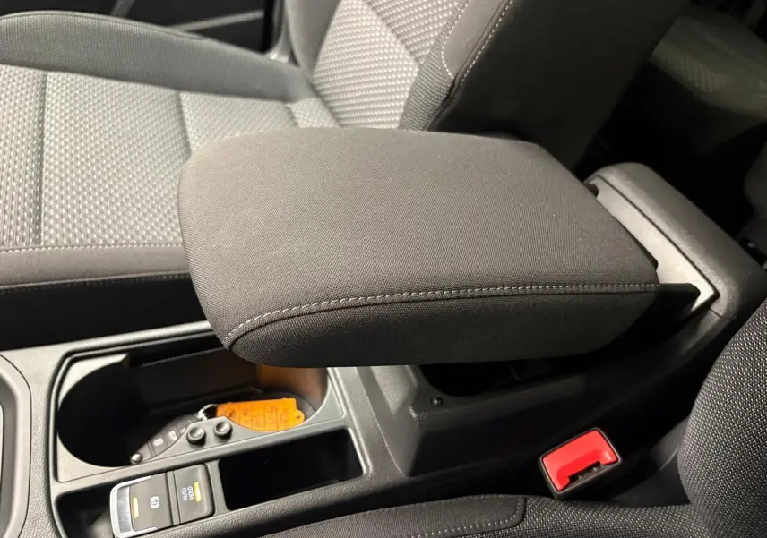 Gros plan sur l'accoudoir central et la console noire intérieure du Volkswagen Touran 2025, tissu gris et détails fonctionnels.
