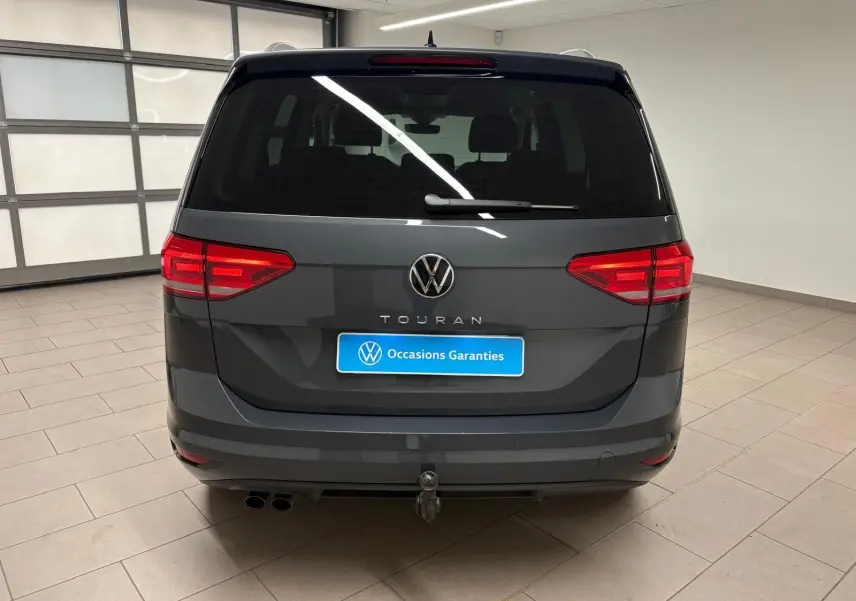 Vue arrière d'un Volkswagen Touran gris dauphin avec attelage escamotable et feux rouges allumés en intérieur.