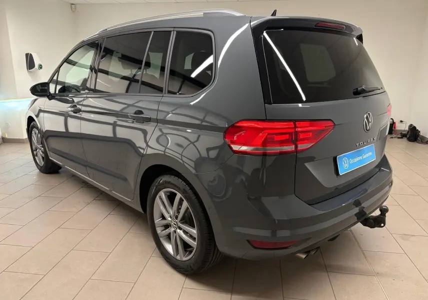Vue 3/4 arrière droite d’un Volkswagen Touran gris dauphin avec attelage escamotable et vitres teintées.