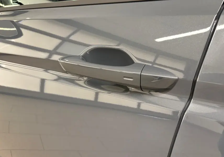 Poignée de porte côté gauche d'un Volkswagen Touran gris dauphin métallisé, vue rapprochée sur la carrosserie lisse.
