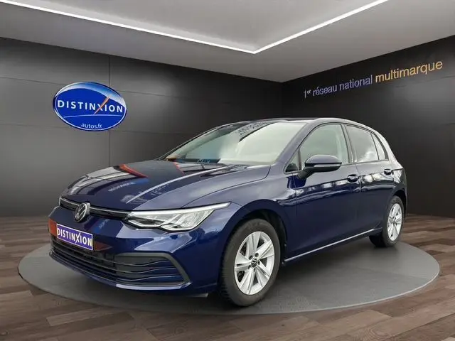 Volkswagen Golf VIII bleu vue 3/4 avant droit en intérieur, avec jantes alliage et calandre moderne lumineuse.