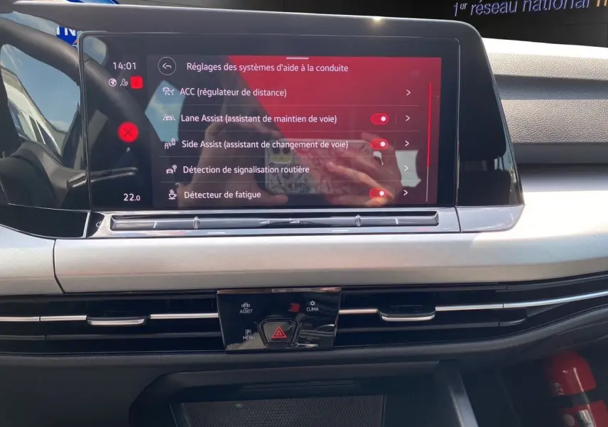 Écran tactile central de la Volkswagen Golf VIII 2023 affichant les réglages d'aides à la conduite dans un intérieur noir.