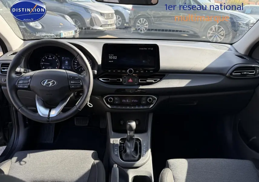 Intérieur de la Hyundai i30 2024 vue de face, tableau de bord noir avec écran tactile et volant multifonction cuir.