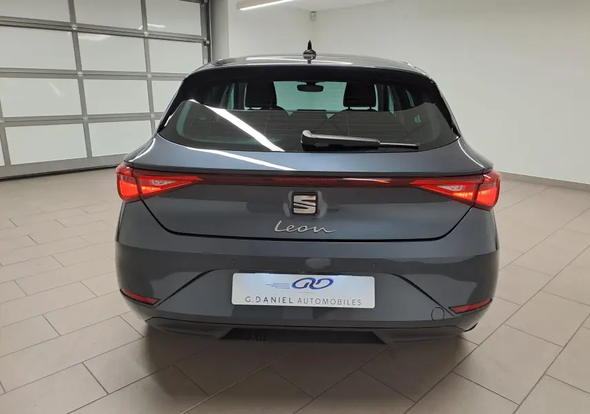 Vue arrière d'une SEAT Leon 1.5 eTSI Hybrid gris magnétique avec vitres arrière surteintées et feux allumés.
